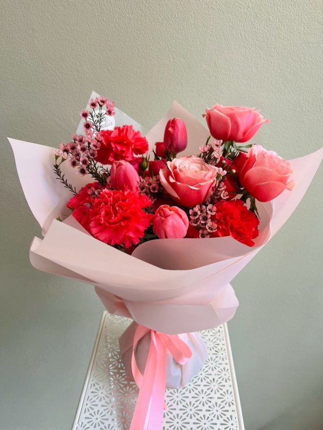 Pink bouquet with roses, tulips, carnations, and waxflowers, wrapped in soft pink paper and tied with a satin ribbon.