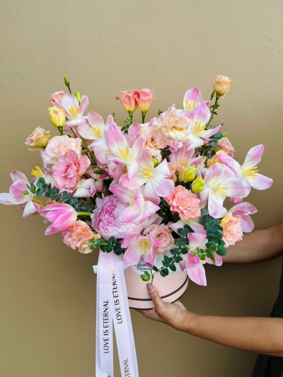 A pastel box filled with pink tulips, carnations, lisianthus, eucalyptus, and a luxurious blush peony at its heart.
