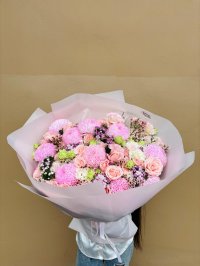 A bouquet of large pink chrysanthemums, roses, and lisianthus with greenery, wrapped in blush pink paper.