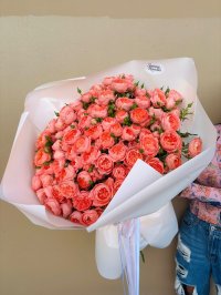 A large bouquet of coral garden roses wrapped in white paper with ribbon.