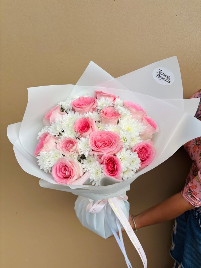 A bouquet of pink roses and white chrysanthemums wrapped in white paper.