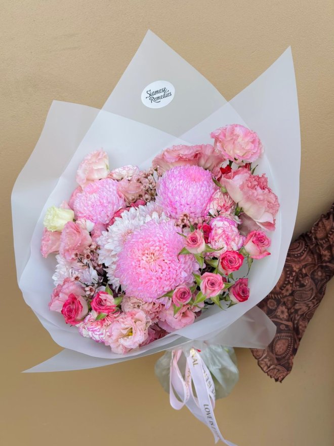 A bouquet of pink chrysanthemums, spray roses, and carnations wrapped in soft white paper.