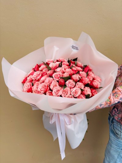 A large bouquet of pink and red roses wrapped in blush paper with white ribbon.