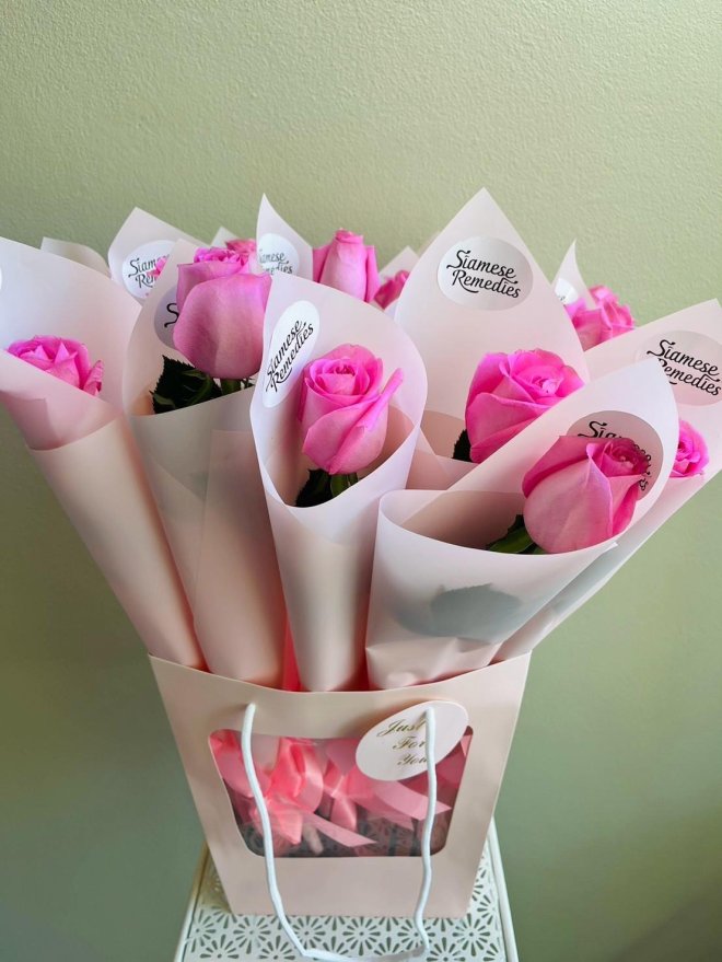 Gift bag filled with individually wrapped pink roses in blush paper, labeled with Siamese Remedies stickers