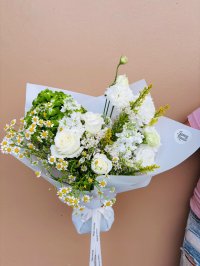 A bouquet featuring white roses, chamomile daisies, lisianthuses, and green hydrangeas wrapped in white paper.