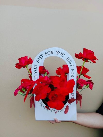 A modern flower box with red roses and carnations arranged inside a white “Just for You” arch handle.