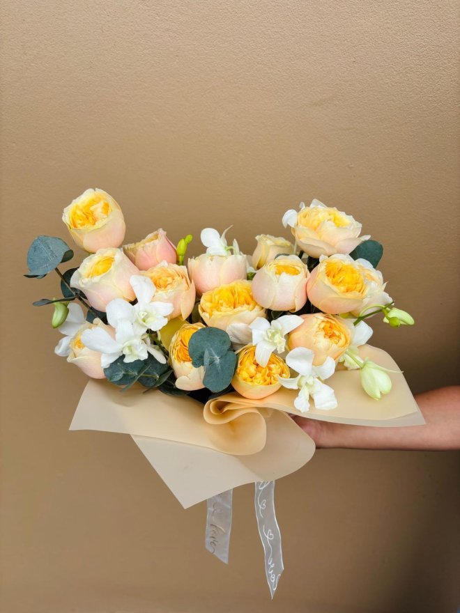 Bouquet of peach garden roses with white orchids and eucalyptus wrapped in beige paper.