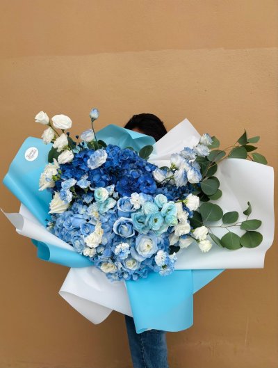A bouquet of blue and white roses and hydrangeas wrapped in elegant blue and white paper.