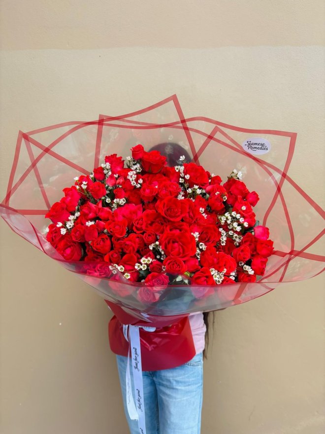 A grand bouquet of red roses accented with baby’s breath, wrapped in red and clear paper.