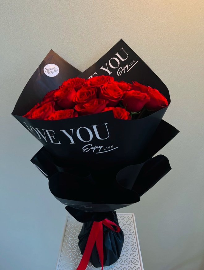 Bouquet of red roses wrapped in bold black paper with “LOVE YOU” printed, tied with a red ribbon.