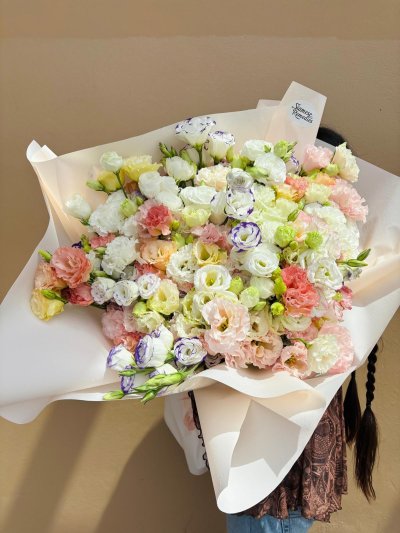 A large pastel bouquet of lisianthuses and carnations in soft pink, peach, white, lemon, and purple tones.