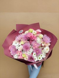 A bouquet of lavender chrysanthemums, pink carnations, and white flowers wrapped in deep plum paper.