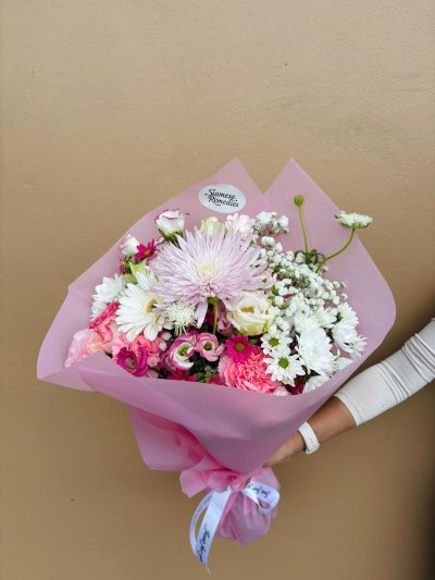 A bouquet of pink carnations, lisianthuses, daisies, and baby’s breath wrapped in pink paper.