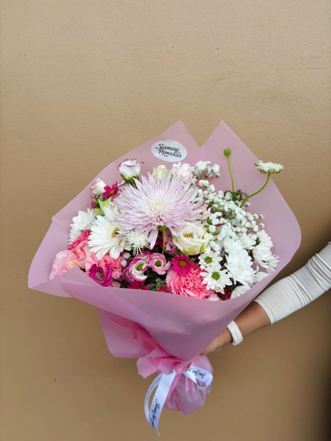 A bouquet of pink carnations, lisianthuses, daisies, and baby’s breath wrapped in pink paper.