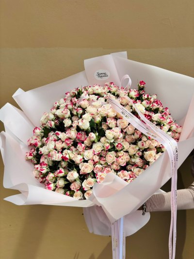 A large bouquet filled with cream and pink two-tone spray roses wrapped in white paper.