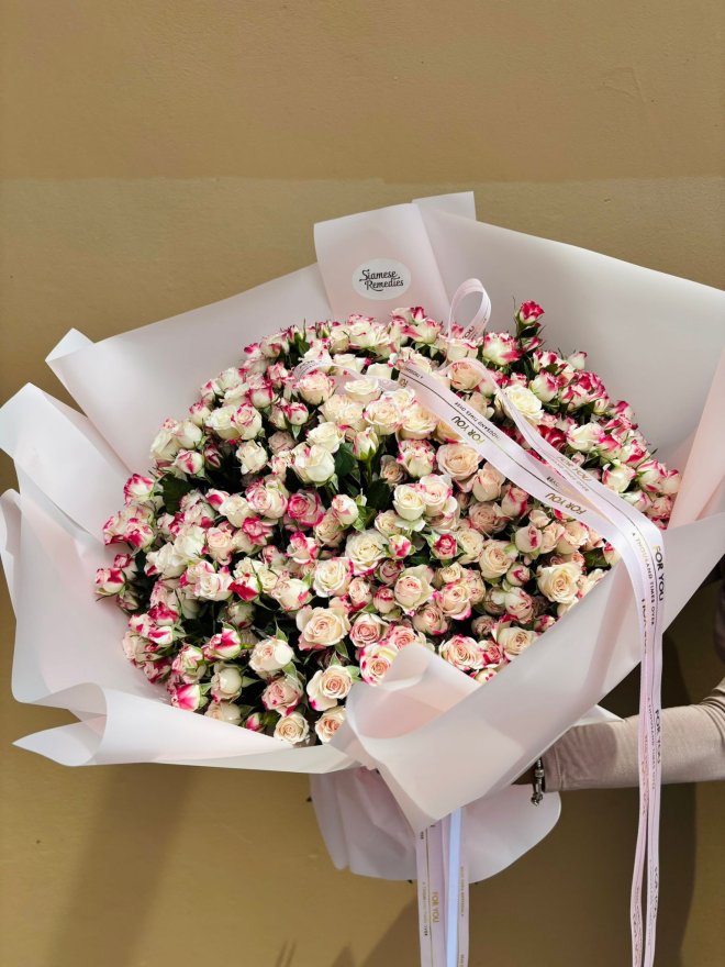 A large bouquet filled with cream and pink two-tone spray roses wrapped in white paper.