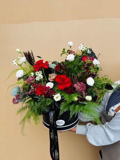 A black hatbox arrangement with red roses, lisianthuses, white blooms, and greenery.