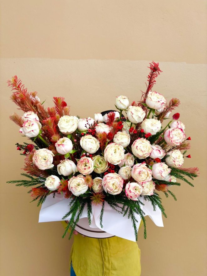 A dramatic bouquet of creamy white roses with crimson accents and greenery, arranged in a wide round display.