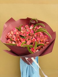 A luxurious bouquet of pink and peach roses with green foliage, wrapped in rose-colored paper.