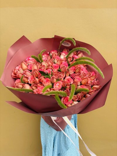 A luxurious bouquet of pink and peach roses with green foliage, wrapped in rose-colored paper.