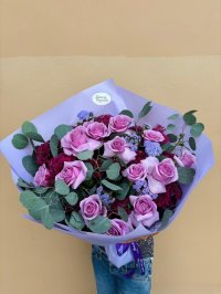 A bouquet of lilac roses, burgundy chrysanthemums, lavender fillers, and eucalyptus wrapped in lavender paper.