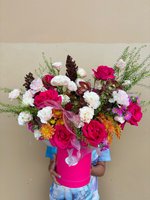 Vibrant Tropic Thunder bouquet held by person in blue clothing, featuring magenta and white roses with orange chrysanthemums in bright pink cylindr...