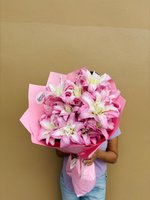 Person holding large bouquet of pink and white lilies wrapped in pink paper against beige wall