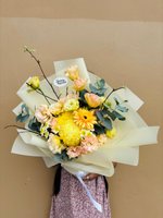 Golden Serenity bouquet with yellow gerberas, chrysanthemums, pink and yellow lisianthus, baby's breath, and eucalyptus wrapped in cream paper