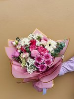 A bouquet of pink chrysanthemums, roses, carnations, and white spider mums wrapped in magenta paper with gold trim.