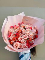 Bouquet of blush and coral roses arranged in soft pink wrapping, resembling a glowing sunrise.