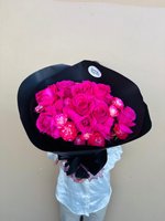 Vibrant magenta and hot pink rose bouquet with spray roses wrapped in black paper, held against a neutral background
