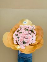Person holding Mimi bouquet of 29 soft pink carnations with ruffled petals wrapped in golden paper against neutral background