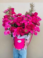 Person holding luxury pink hatbox filled with vibrant pink and magenta roses, gerberas, and spray roses in an elegant floral arrangement