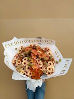 Bouquet of burnt orange, golden beige, and cream chrysanthemums wrapped in white paper with gold lettering.
