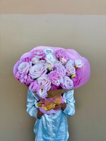 Person holding Juliet bouquet with pink and white roses and lisianthus wrapped in pink tissue paper with golden ribbon