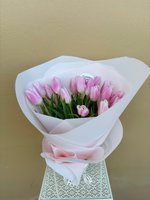 Fifteen soft pink tulips arranged in a hand-tied bouquet, wrapped in white tissue paper with a pink ribbon, displayed against a neutral beige backg...