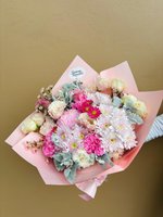 A pastel bouquet of pink, white, and purple flowers with eucalyptus wrapped in white paper.