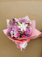 A bouquet of pink chrysanthemums, roses, and white lilies wrapped in pink paper.