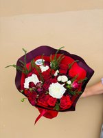 Hand holding Navida bouquet with white roses, red roses, and burgundy spray roses wrapped in dark burgundy paper with evergreen accents
