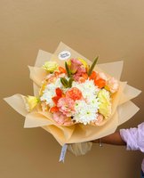 A bouquet of orange lilies, white chrysanthemums, yellow lisianthus, and peach carnations wrapped in golden paper.