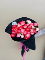Carmen bouquet featuring 25 mixed red, pink and white ranunculus flowers wrapped in black paper with pink ribbon, held by hand