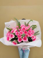 Lucy bouquet featuring pink roses with white edges wrapped in white paper, held by person in jeans against beige wall