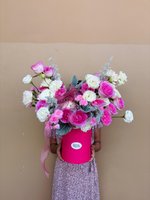Elegant pink hatbox arrangement with pink and white roses, white carnations, and silvery foliage held by person in floral dress