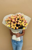 Person holding large bouquet of 60 yellow roses with red-pink edges wrapped in white paper against beige background