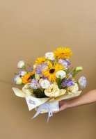 Vincent bouquet with sunflowers, white lisianthus, and lavender blooms wrapped in pale yellow paper.