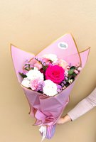 Hand holding Tina bouquet with bright magenta rose, white lisianthus, pink carnations, purple statice and baby's breath in pink wrapping