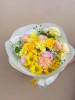 Sandra bouquet featuring yellow roses, pink and white carnations, yellow chrysanthemums, and white baby's breath wrapped in white paper with yellow...
