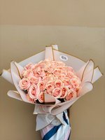 Bouquet of peach-pink roses wrapped in soft white paper with golden trim.