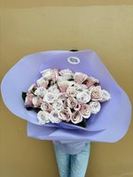 Large bouquet of 39 pale pink and white roses wrapped in purple paper, held by person in light blue jeans against beige wall