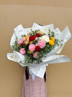Garden Jubilee bouquet featuring twelve mixed ranunculus flowers in pink, red, white, and yellow colors with green foliage, wrapped in white paper...